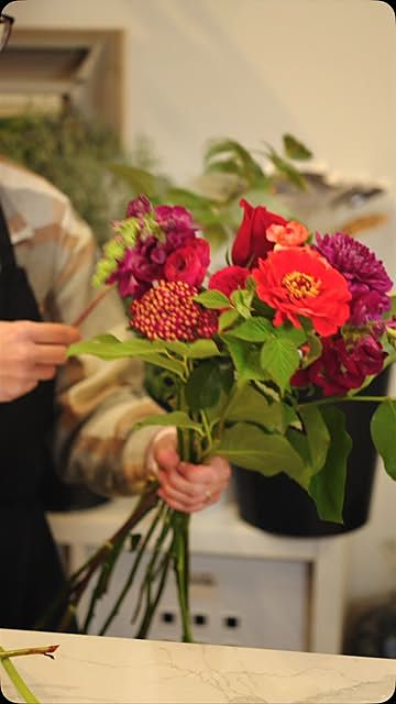 A florist's hands holding a freshly tied bouquet of red and pink flowers