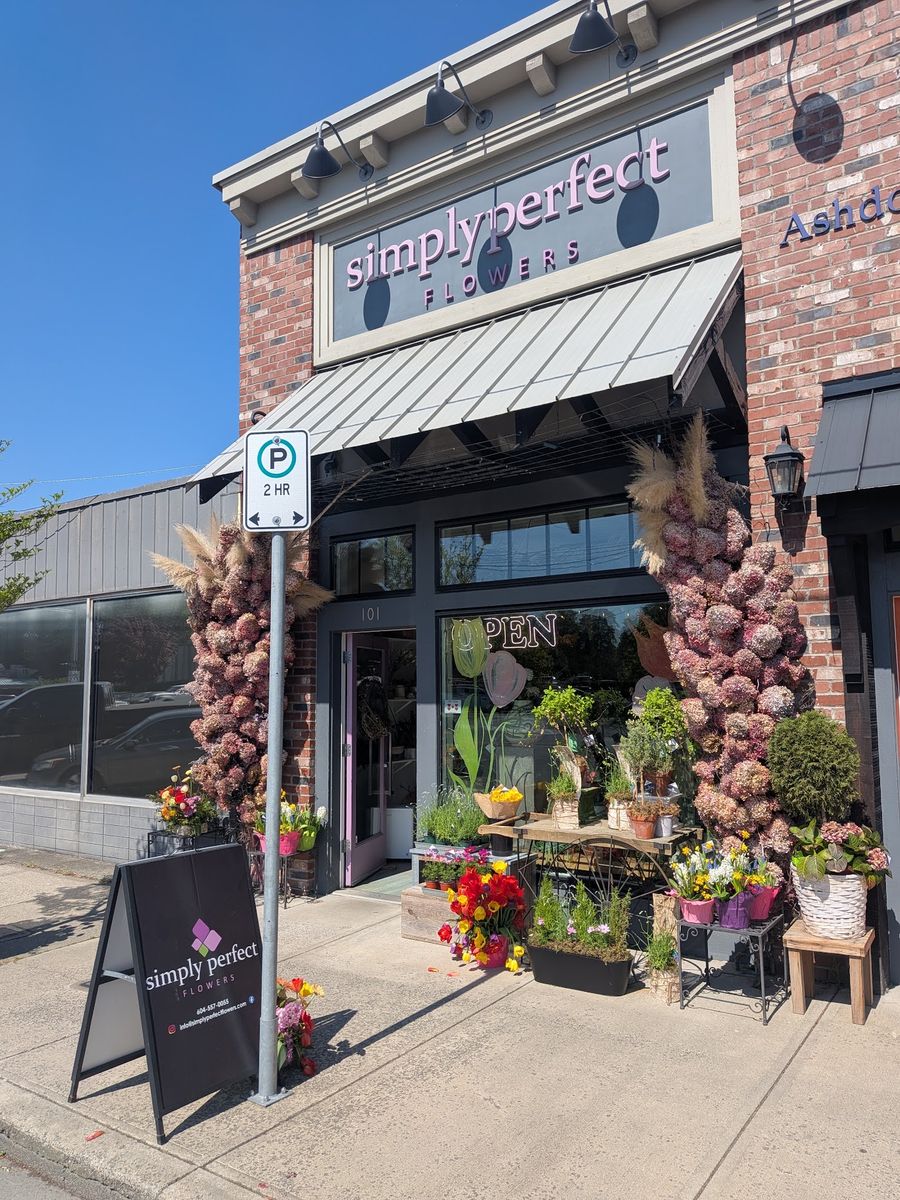 The shop by day, with flowers and plants on the sidewalk and a sandwich-board sign
