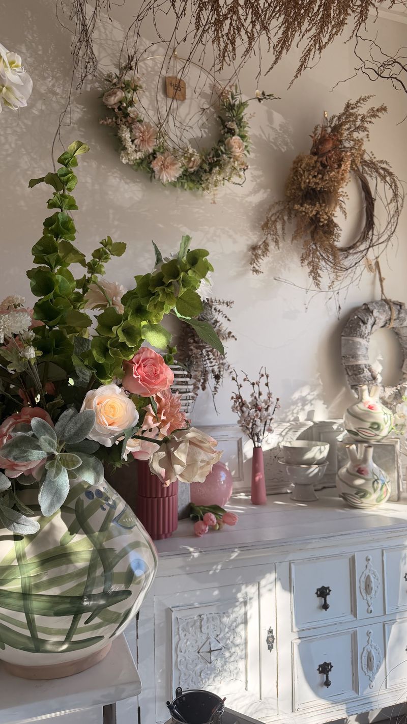 Shop wall with dried wreaths above a vintage white dresser and fresh arrangements